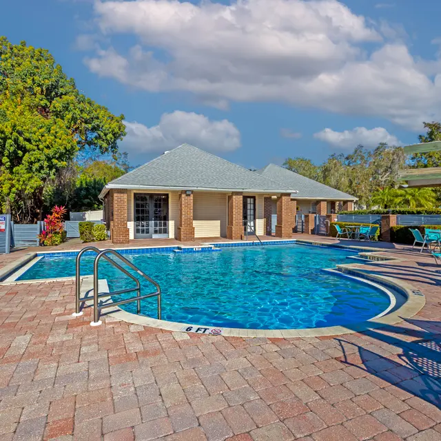 A swimming pool area with lounge chairs, surrounded by lush greenery and a building in the background.