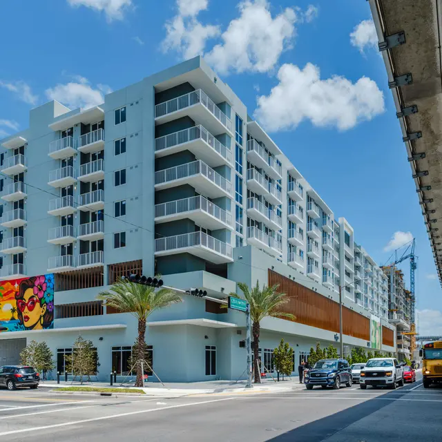 A modern apartment building with a colorful mural on the side, surrounded by palm trees and vehicles on a sunny day in Miami.