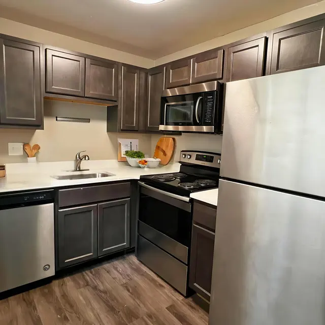 A modern kitchen featuring dark wood cabinets, stainless steel appliances, and a bright countertop with various kitchen tools and decor.