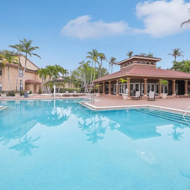 A clear blue swimming pool surrounded by palm trees, lounge chairs, and a poolside cabana.