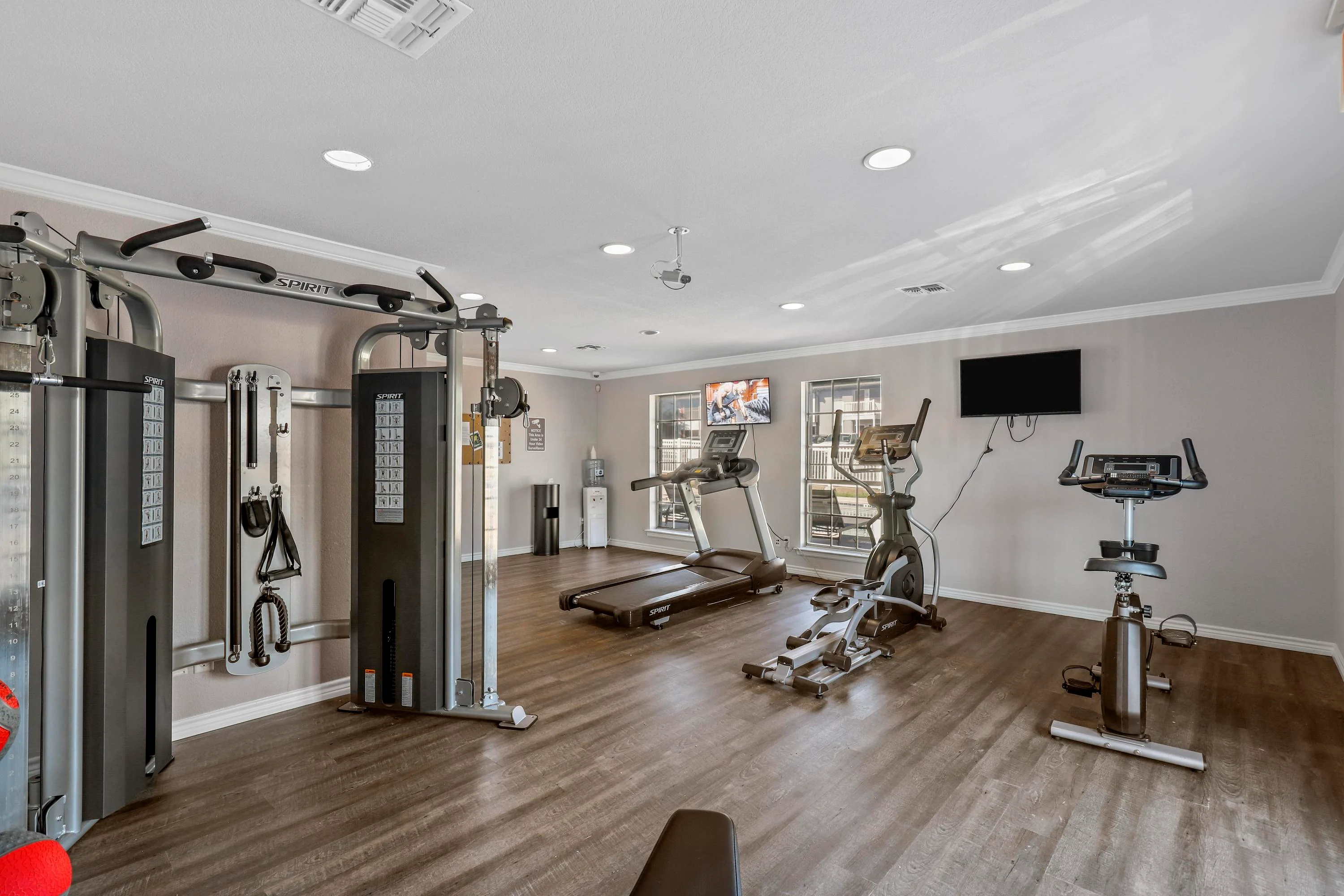 A modern gym interior featuring various exercise machines and equipment, including weight machines, a treadmill, and a stationary bike, with a flat-screen TV mounted on the wall.