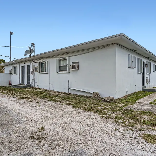 A side view of a white apartment complex with multiple windows, grass, and a gravel path.
