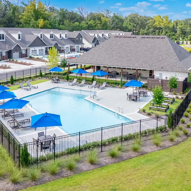 Residential Swimming Pool Area Aerial view of a modern residential swimming pool area surrounded by green lawns, lounge chairs, and umbrellas.