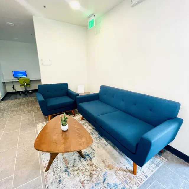 Modern Living Room Setup A cozy living area featuring a blue sofa and chair with wooden legs, a small round coffee table, and a decorative rug on the tiled floor.