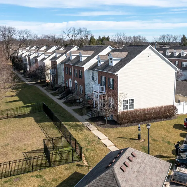 Aerial view of a residential apartment complex with multiple buildings, a grassy area, and parked cars.