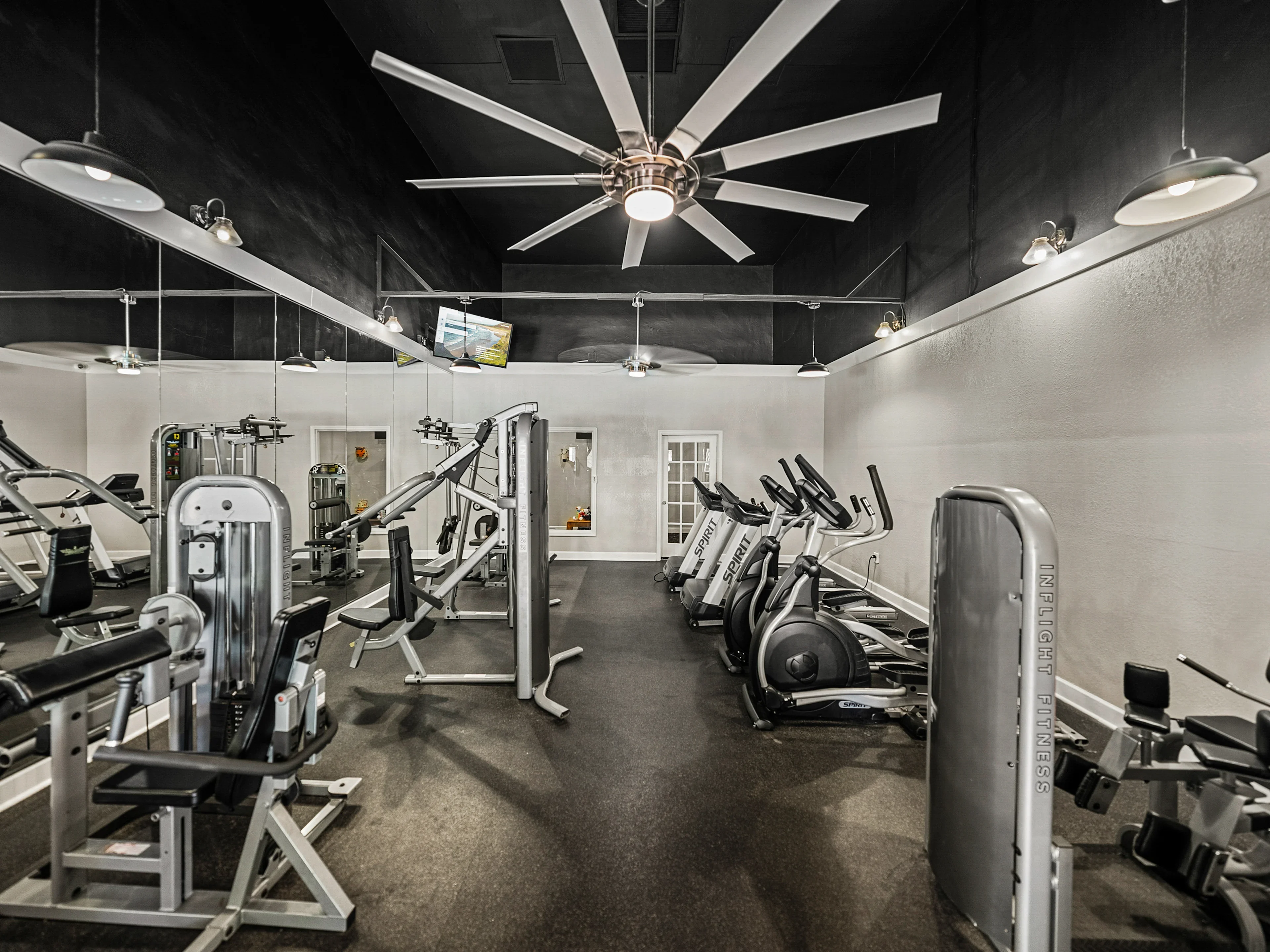 Interior view of a gym with exercise machines and a large ceiling fan.