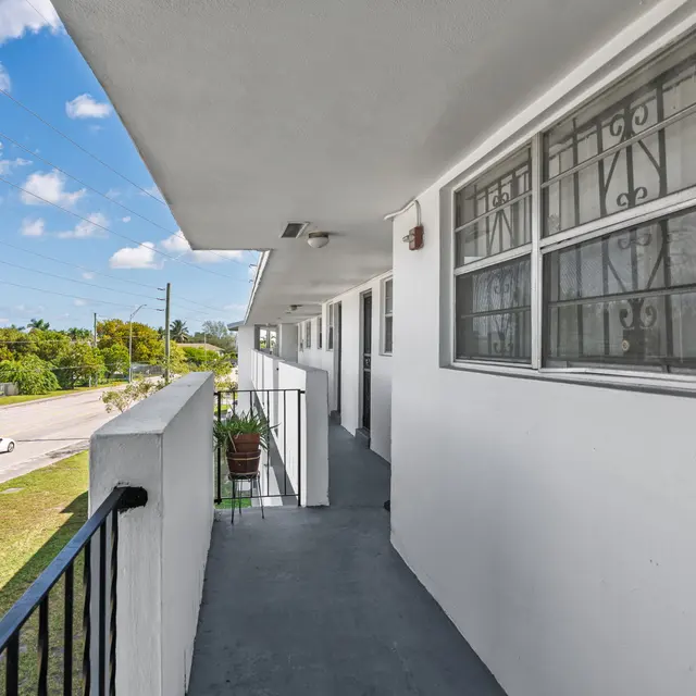 A view of a corridor in an apartment building with a balcony overlooking a road and greenery.