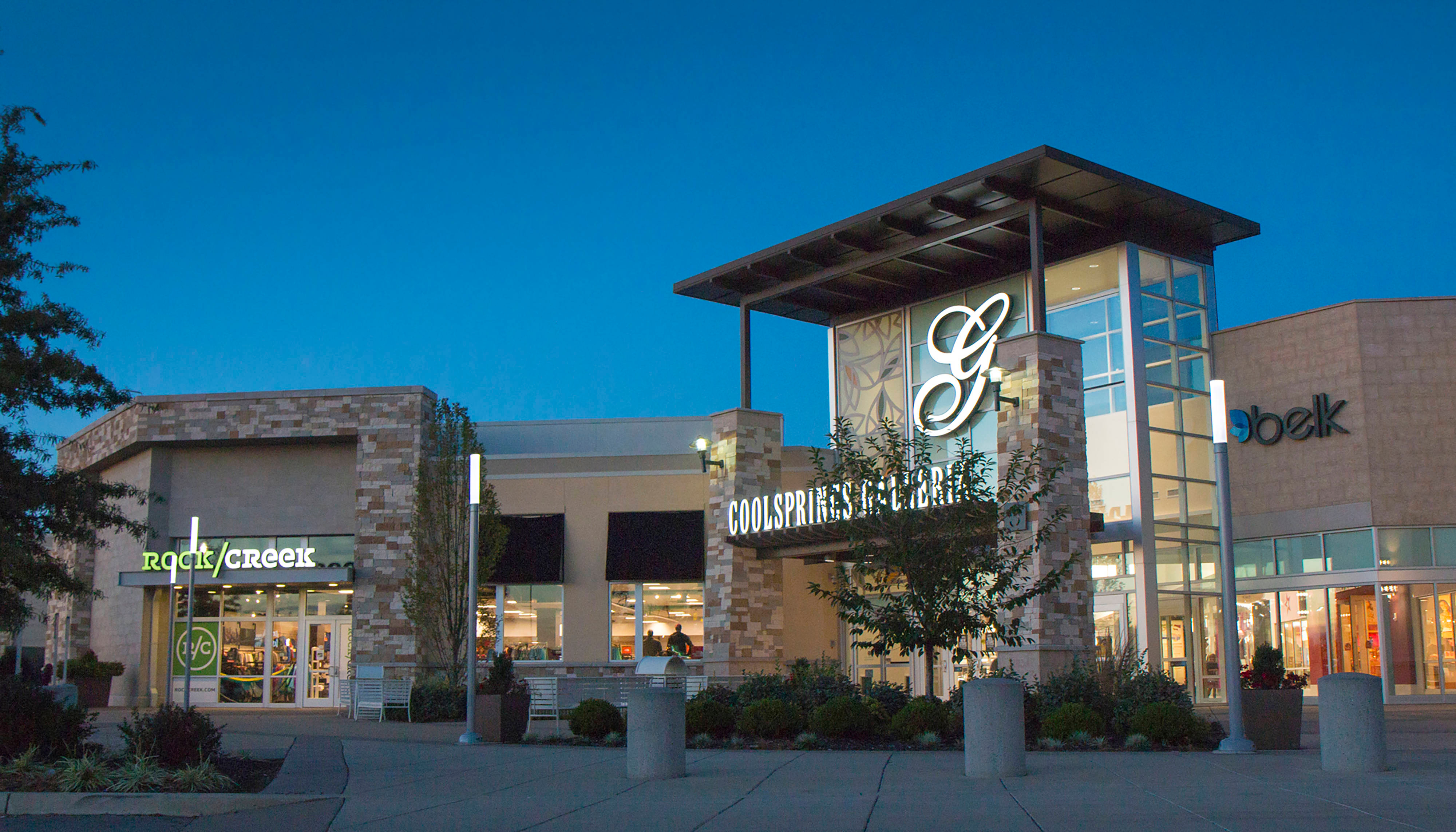Exterior view of Cool Springs Galleria shopping mall at dusk, showcasing stores and landscaping.