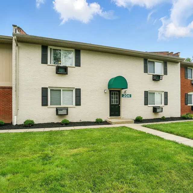 Exterior view of a two-story apartment building with a mix of brick and painted walls, featuring green awnings above windows and doors.