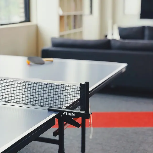 A ping pong table with a net, situated in a room featuring a gray couch and bookshelves.