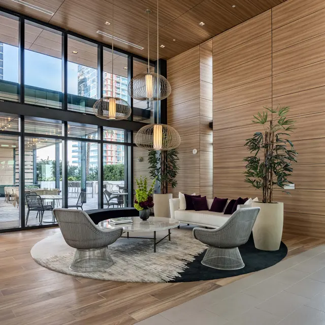 A stylish modern lobby with wooden walls and large windows, featuring a round rug, a white sofa, and several decorative plants.