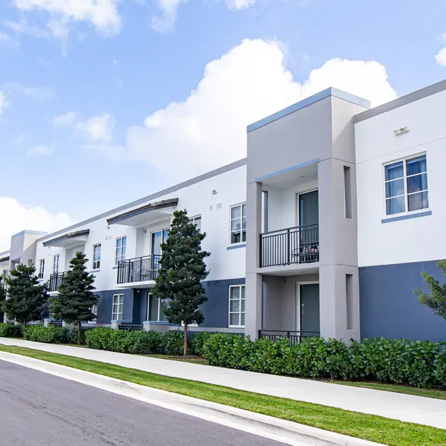 Modern Apartment Complex View of a modern apartment building with trees and greenery along a sidewalk.