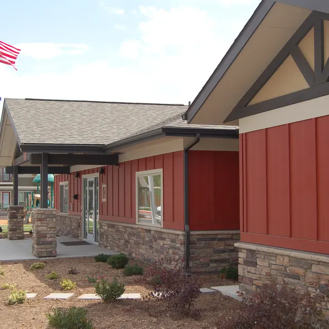 Modern Building Exterior with Flags Exterior view of a modern building with red and stone facade, featuring a blue flag and an American flag flying frontally, with a landscaped pathway.
