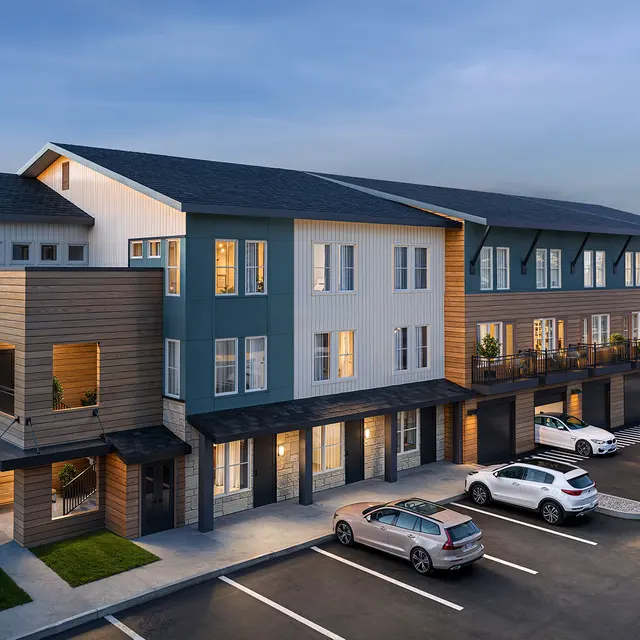 A modern multi-unit apartment building with a combination of light and dark exteriors, surrounded by several parked cars.