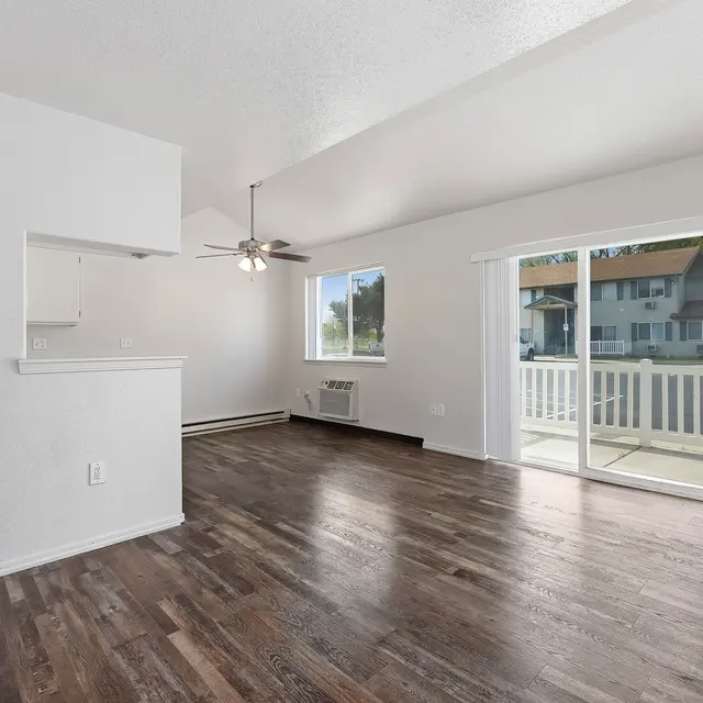 Spacious Living Room A spacious and bright living room with large windows, a ceiling fan, and a sliding glass door leading to a balcony. The floor is wood laminate, and the walls are painted a light color.