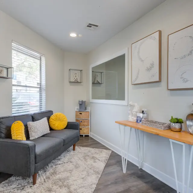 A modern living room with a gray sofa, two yellow cushions, a cozy rug, a wooden side table with decorations, and abstract wall art.