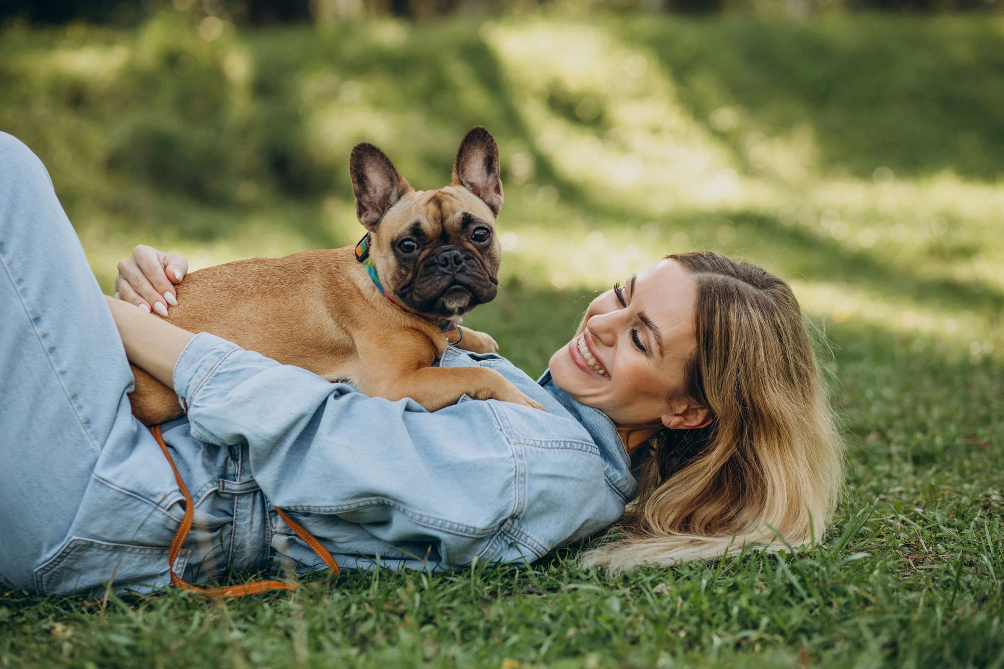 Joyful Moment with a French Bulldog A woman lying on grass with a French Bulldog on her lap, smiling at the camera.