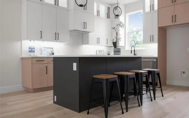 A contemporary kitchen featuring a black island with wooden stools, white and light wood cabinetry, and modern pendant lights.