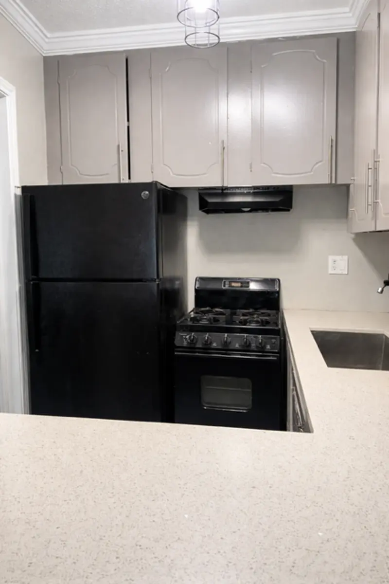 A modern kitchen featuring a black refrigerator, black stove, and light gray cabinets, with a countertop made of a light-colored material.