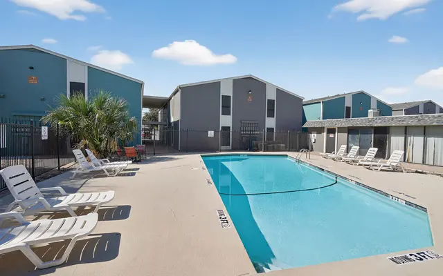 Swimming pool surrounded by lounge chairs and residential buildings in the background.