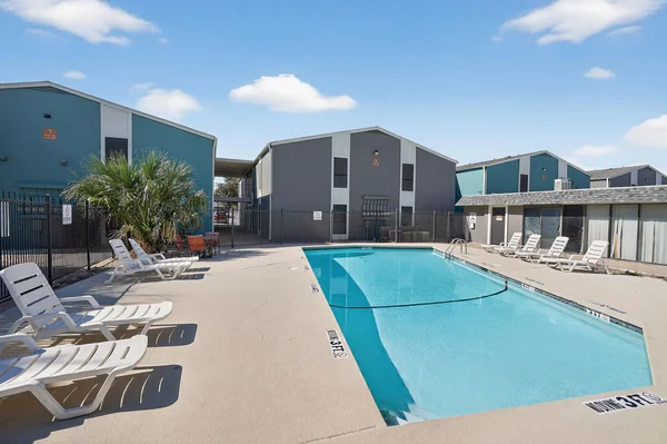 Swimming pool surrounded by lounge chairs and residential buildings in the background.