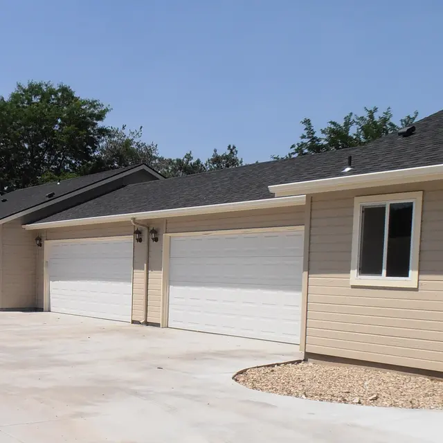Row of new beige houses with garages and a clear blue sky.