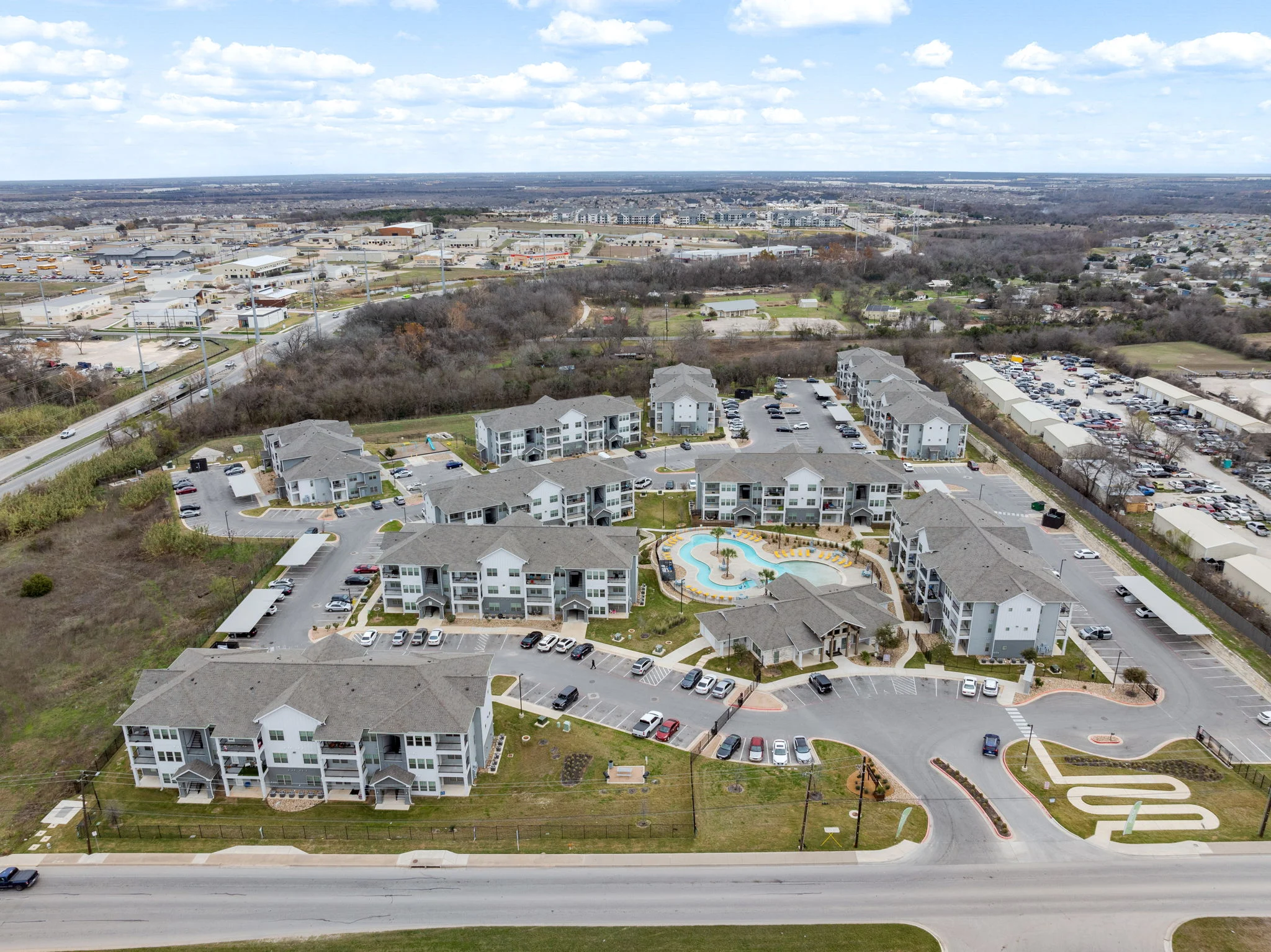 Aerial view of a modern apartment complex featuring several buildings and a central pool area.