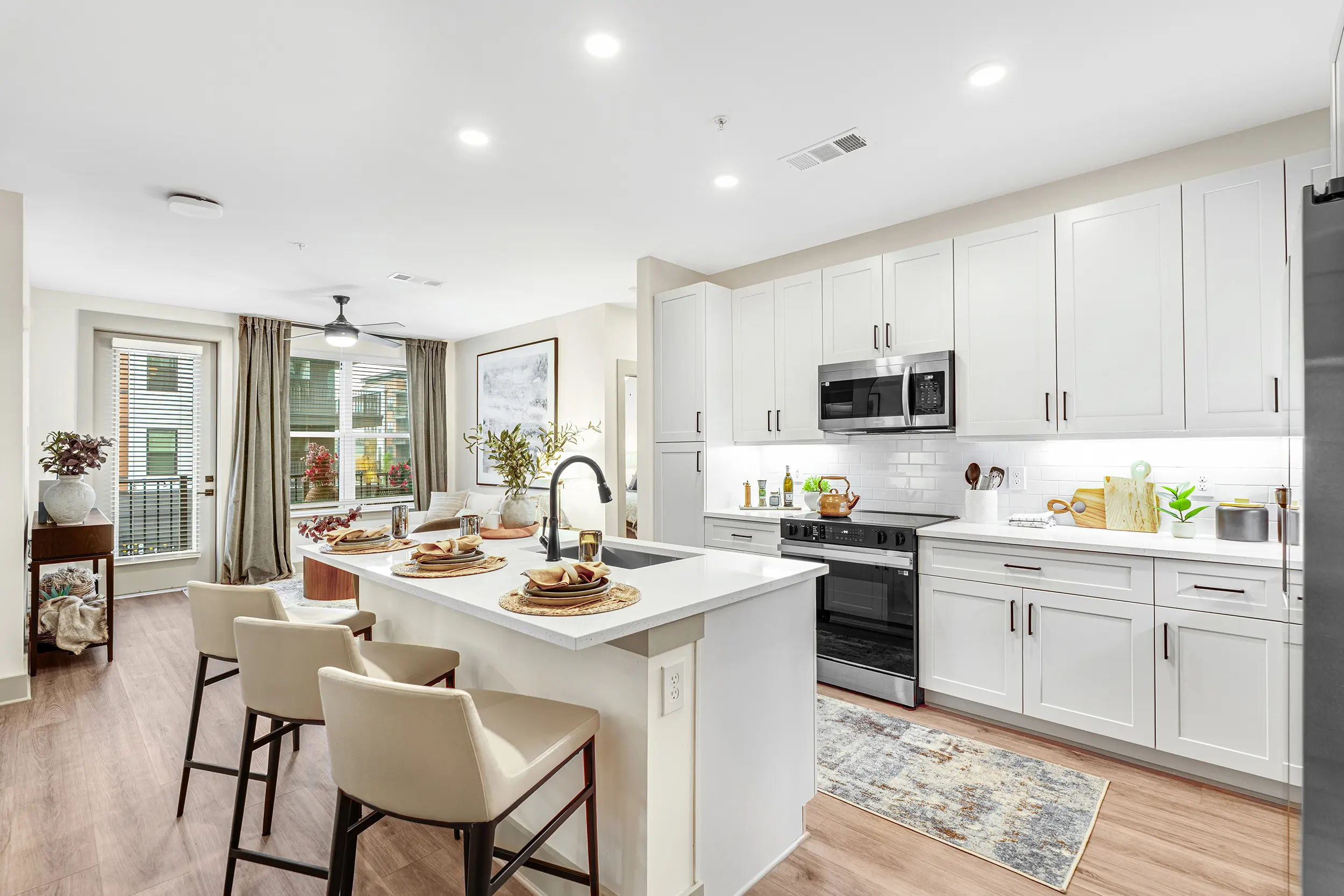 Bright and modern kitchen featuring white cabinetry, a large island with seating, and a view of the outdoor balcony through glass doors.