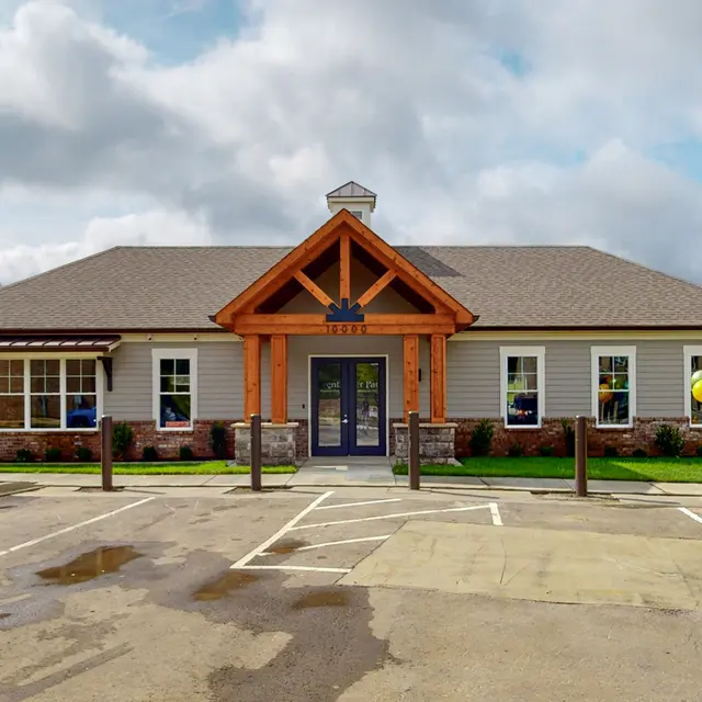 The exterior of a community center featuring a wooden entryway, large windows, and a parking lot in front.