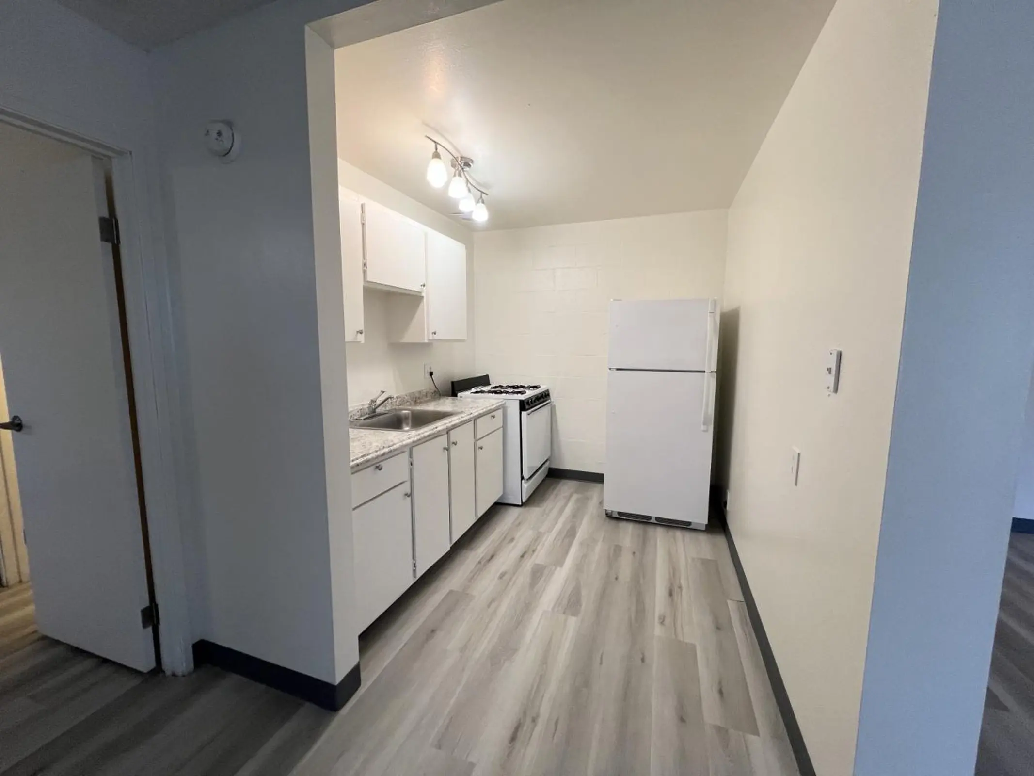 Kitchen viewed toward the stove and refrigerator, with white cabinets.