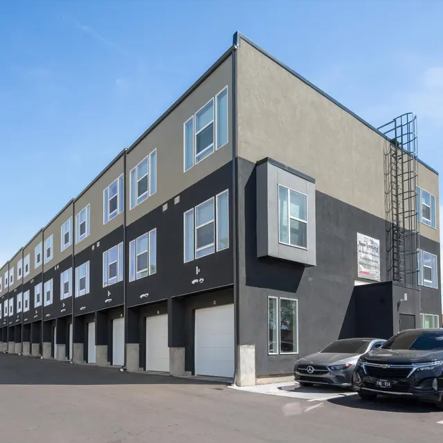 A modern multi-story building with a dark exterior and large windows, featuring several parking spaces in front.