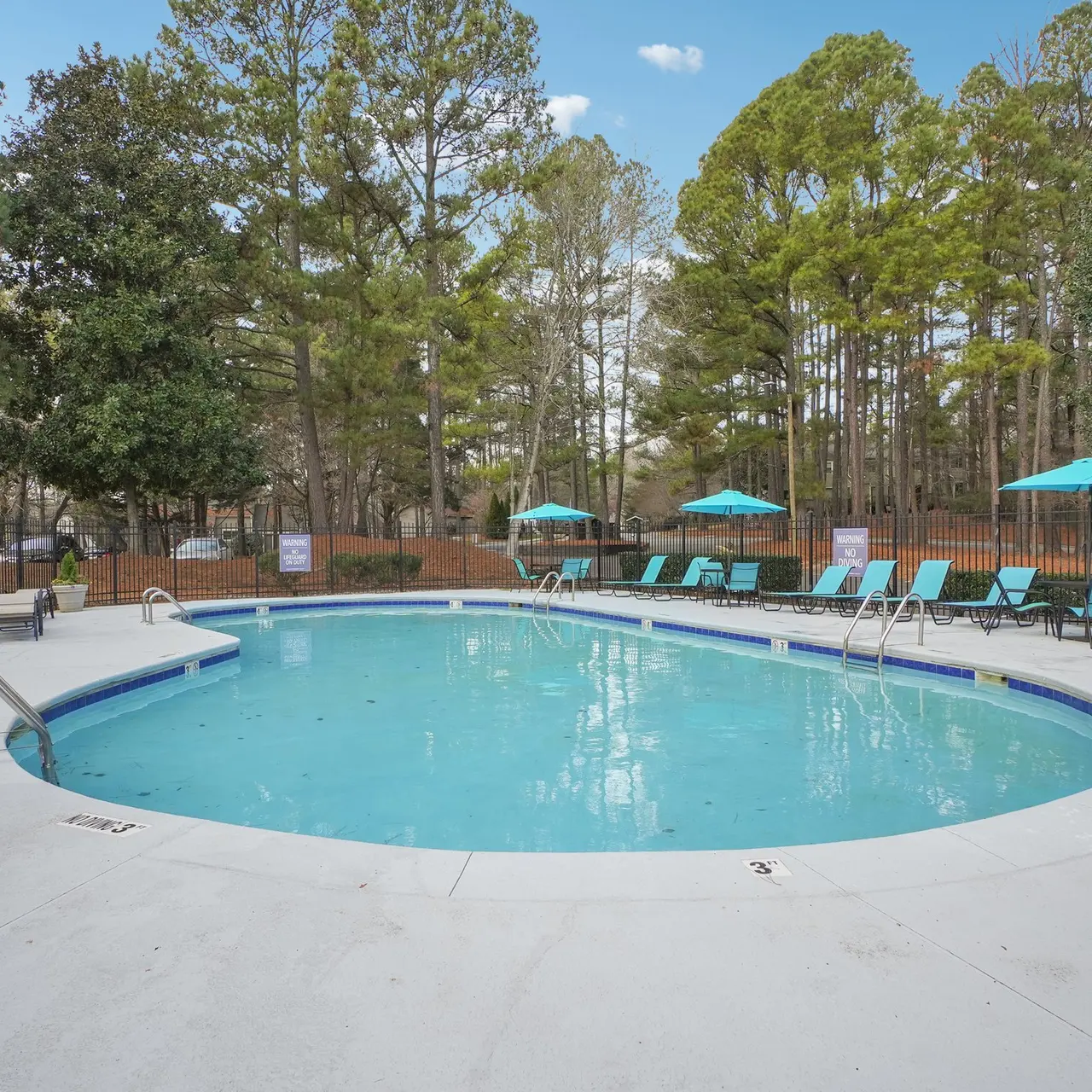 A serene swimming pool surrounded by trees and lounge chairs with umbrellas.