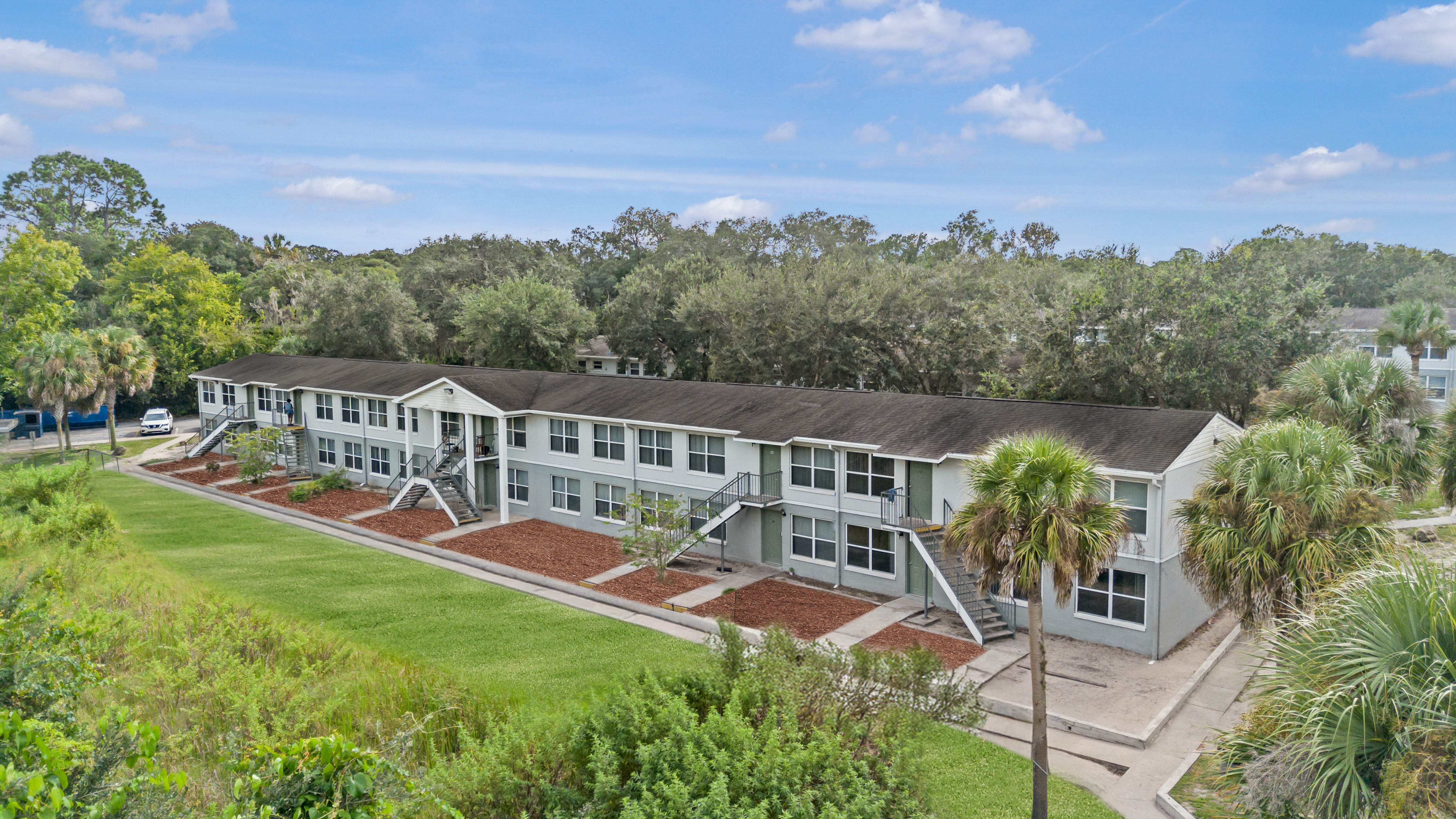 Modern Apartment Complex View of a modern apartment complex surrounded by greenery and palm trees under a clear blue sky.