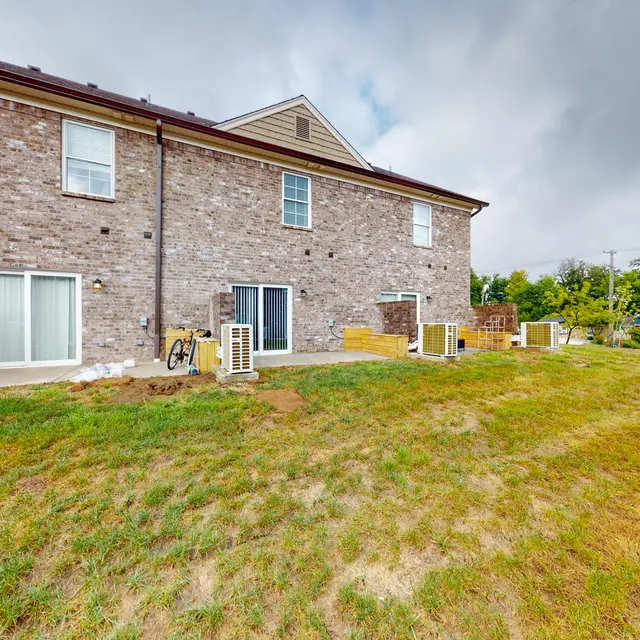View of the back side of a residential building with a grassy yard and air conditioning units.