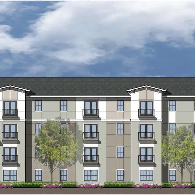 Architectural rendering of a modern apartment building with multiple stories, featuring a blend of tan, white, and dark blue colors, surrounded by trees and purple flowers, under a partly cloudy sky.