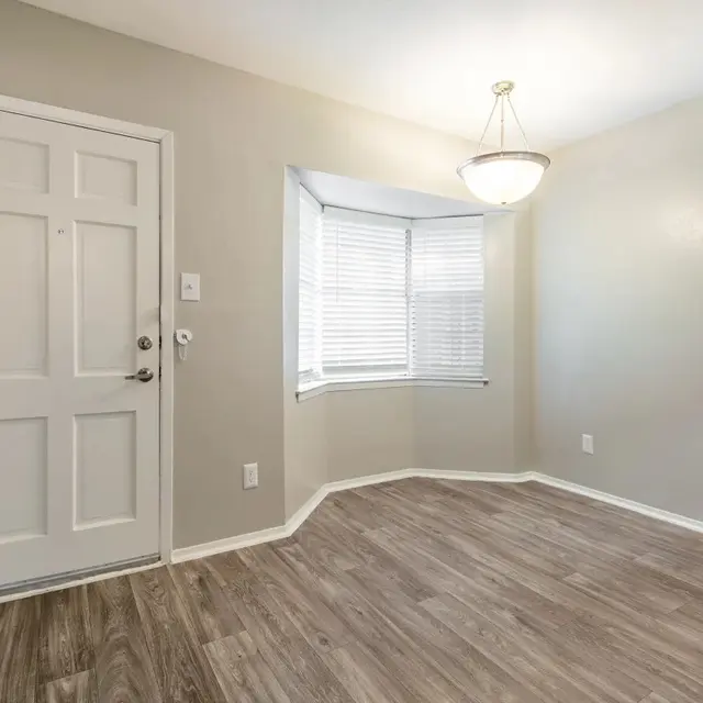 Light-filled corner of a room featuring a front door, bay window with blinds, and laminate flooring.