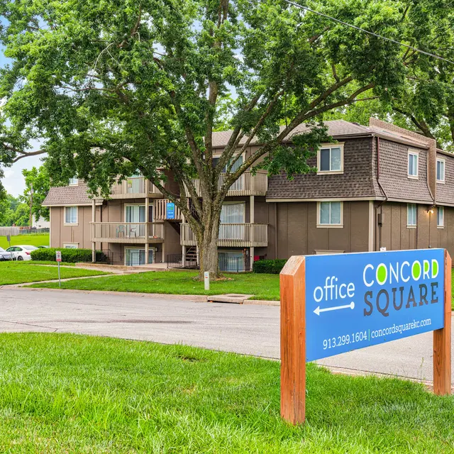 Sign and view of a residential apartment complex called Concord Square, with green grass and trees around.