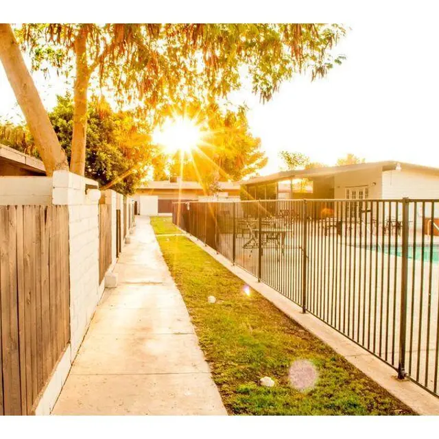 Sunset by the Poolside A sunlit pathway next to a fenced pool area, with trees and residential buildings in the background.