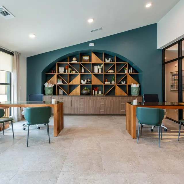 Interior view of a modern office lobby featuring wooden tables and green chairs, with a decorative shelf in the background.