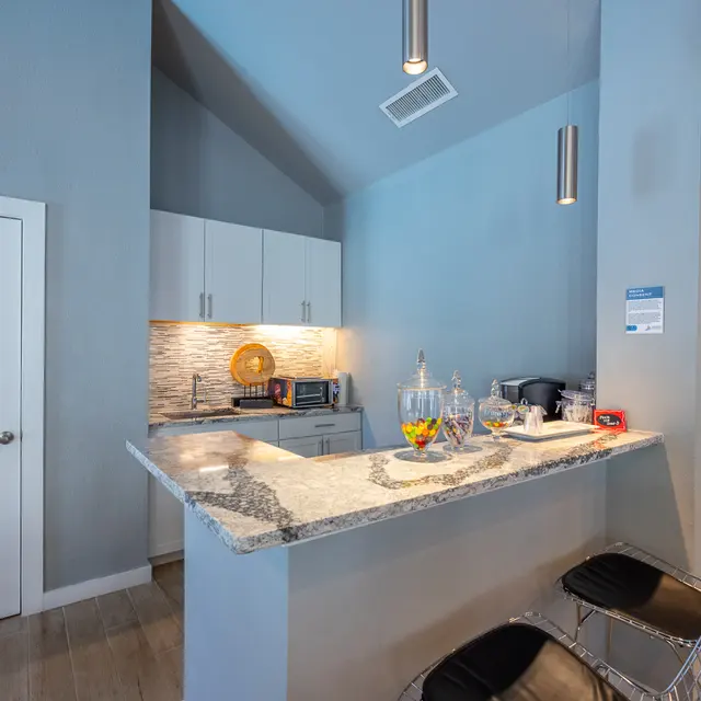 Modern Kitchen Interior A modern kitchen space featuring a grey color scheme, a granite countertop, white cabinets, and stainless steel appliances. Two stylish bar stools are positioned at the counter, and there's ambient lighting from pendant lamps above.