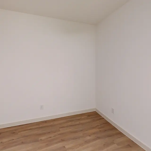 An empty room with neutral white walls and wooden flooring.