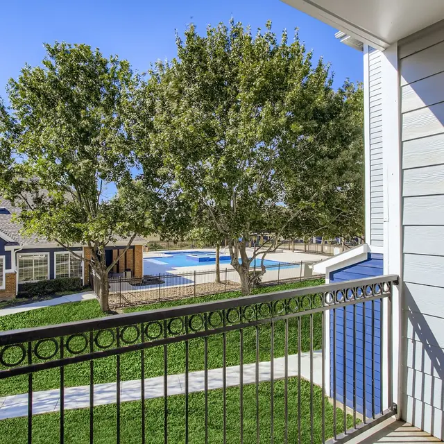 View from an apartment balcony overlooking a landscaped area with trees and a swimming pool
