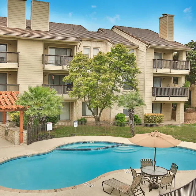 View of an apartment complex with a swimming pool surrounded by palm trees and lounge furniture.