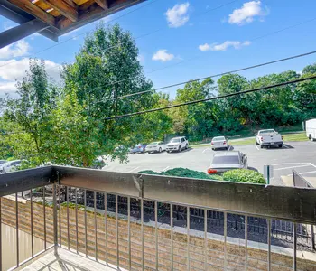 View from a balcony looking out over a parking lot with trees and blue sky.