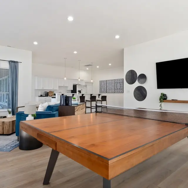 Monterra Townhomes - Spacious Modern Living Area A spacious modern living area featuring a large wooden table, comfortable seating, and a fireplace. The decor includes blue curtains, a wall-mounted television, and decorative circular wall pieces.