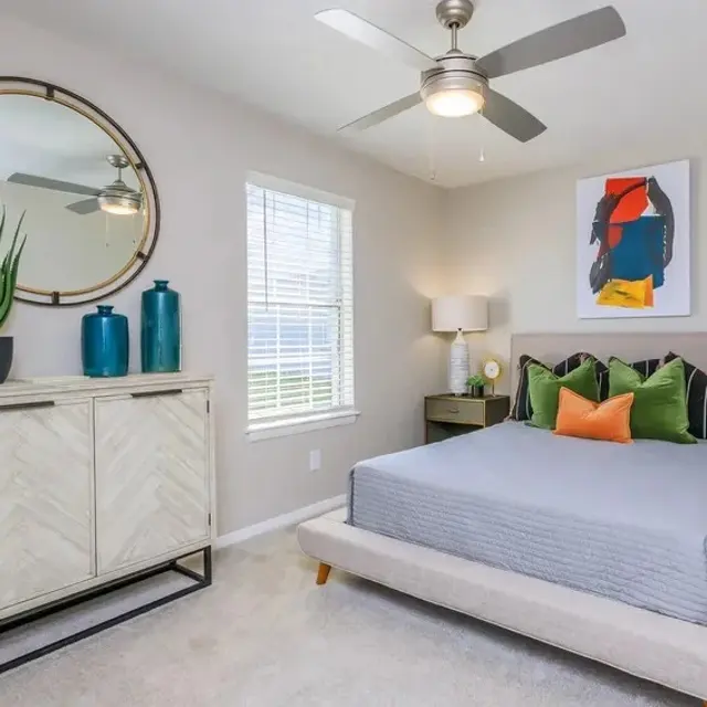 Modern bedroom featuring a neutral palette, a large round mirror, decorative vases, and a stylish bed with colorful pillows.