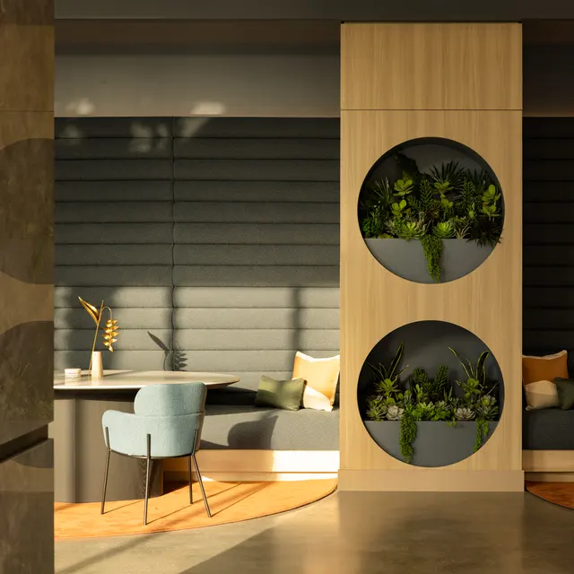 A modern interior space featuring a wooden partition with circular planters, seating area with cushions, and soft lighting.