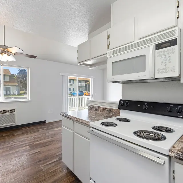 Open Concept Kitchen and Living Room A modern kitchen with a stove and microwave, featuring granite countertops and a fan, looking into a living area with laminate flooring and large windows.