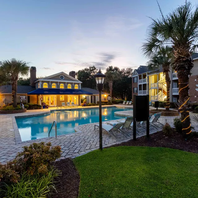 Evening view of a modern apartment complex pool area with palm trees and outdoor seating