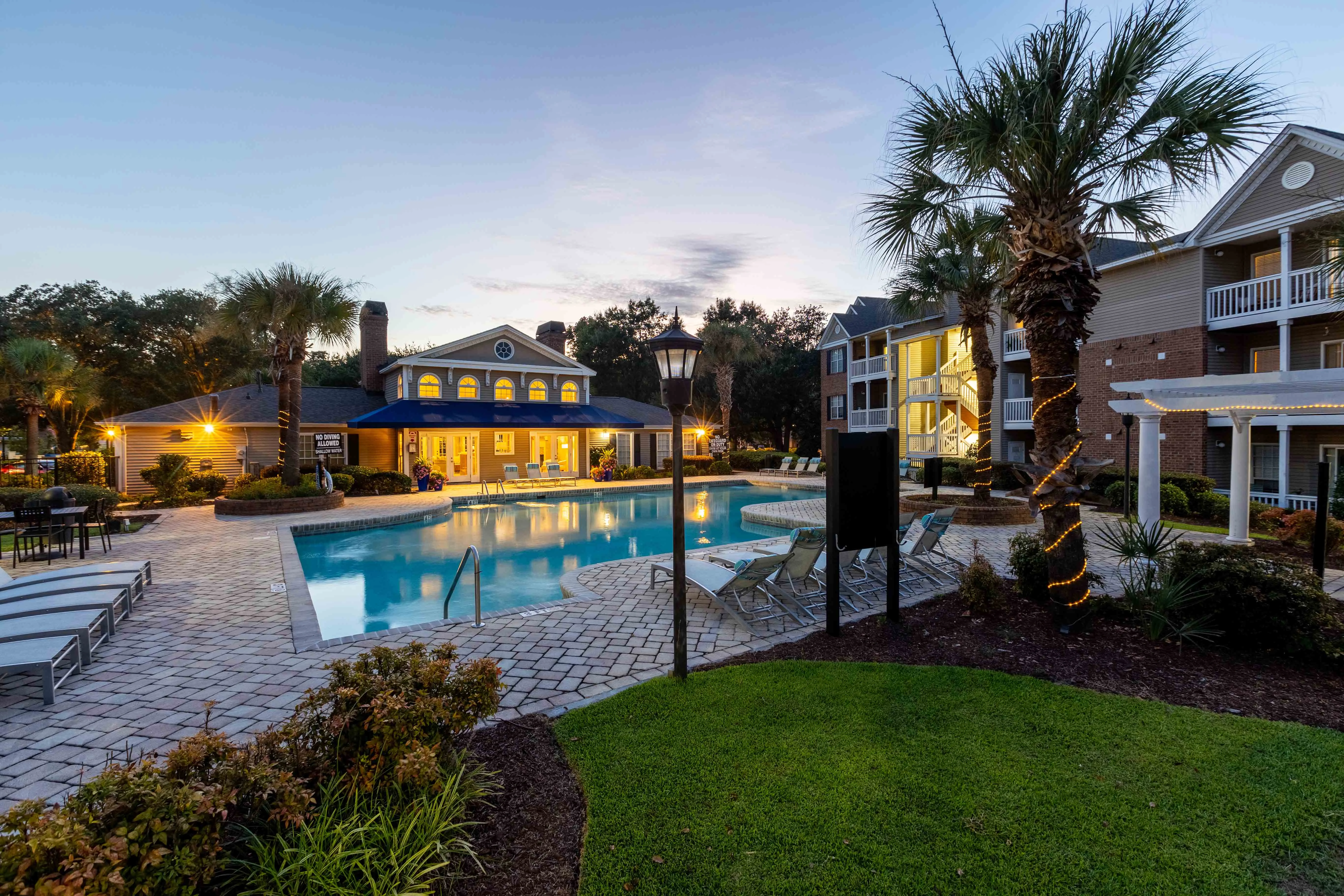 Evening view of a modern apartment complex pool area with palm trees and outdoor seating